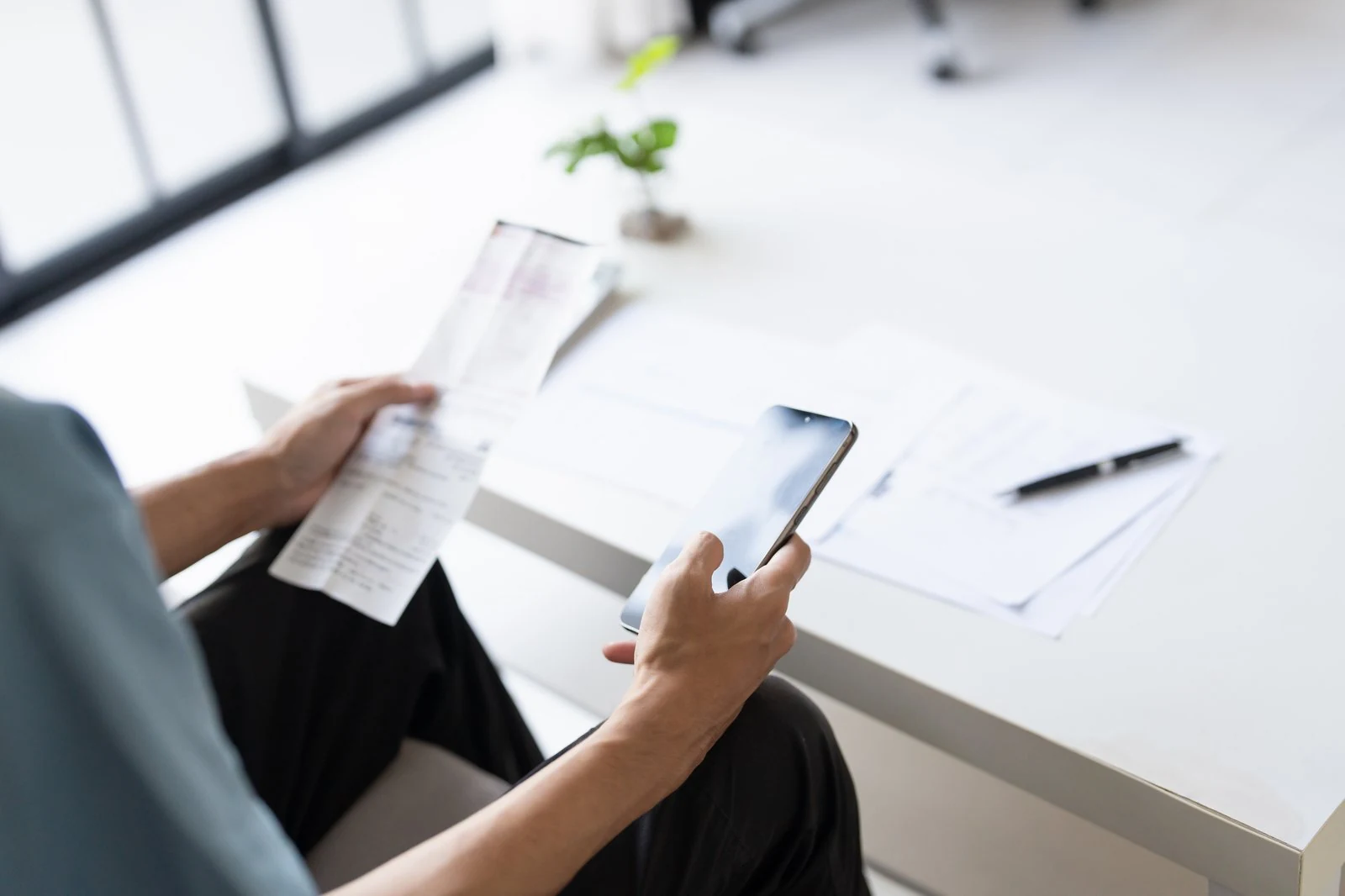 En person med kvittering og mobiltelefon ved et skrivebord